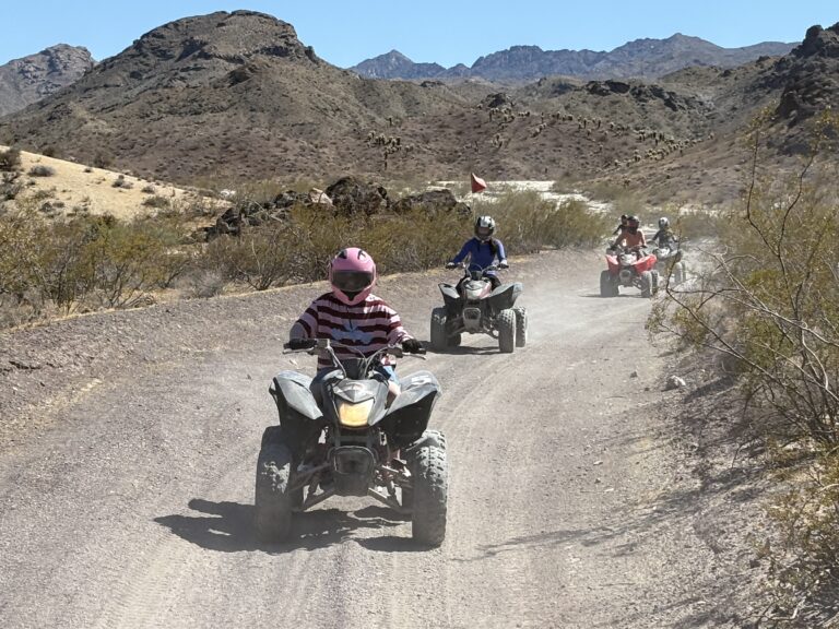 Group enjoying an ATV tour near Las Vegas, Nevada, riding dusty desert trails surrounded by rocky hills and sparse plants.