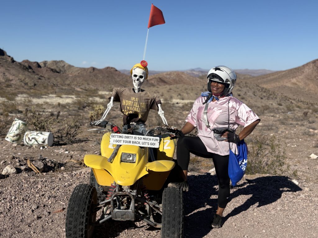 Helmeted woman poses beside a yellow ATV and skeleton on a Nevada desert trail, ideal for Las Vegas ATV tours and Ghost Town rides.