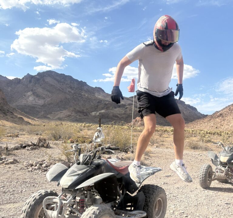 Adventurer in helmet and gear jumps off ATV during a Nevada desert ATV tour near Las Vegas with mountains in the background.