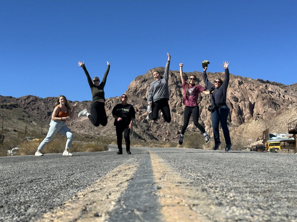 Group at Nelson Ghost Town near Las Vegas, Nevada, jumping and smiling on a desert road—adventure by Colorado River.
