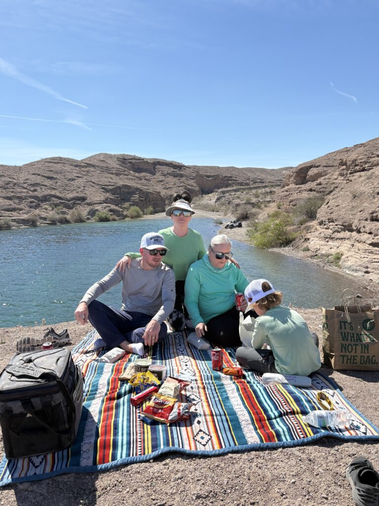 Family enjoys snacks on a blanket by the Colorado River near Las Vegas, Nevada, after a day of ATV and Ghost Town sightseeing.