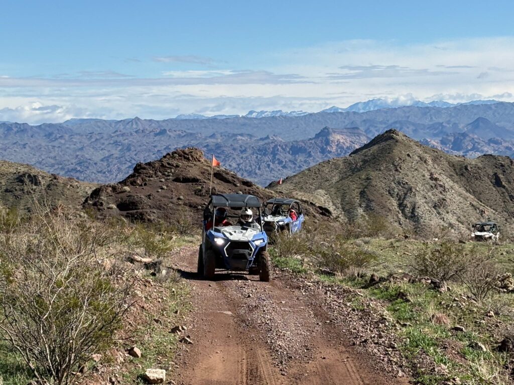 ATVs on a rugged Nevada desert trail near Las Vegas with mountains, blue sky, and green patches—perfect for ATV tours or RZR rides.