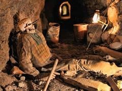 Skeleton in tattered clothes slumps in Nevada tunnel with mining tools—evokes Las Vegas Ghost Town sightseeing adventure.