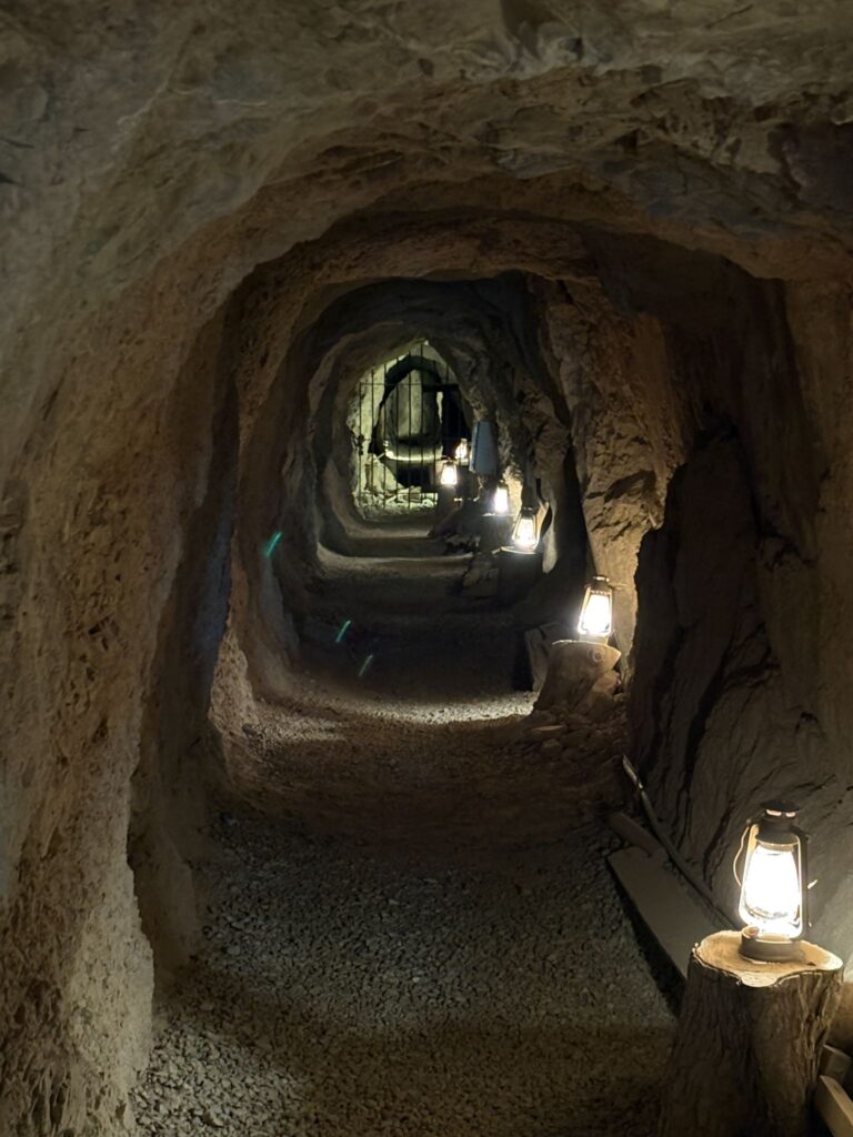Explore a dimly lit Nevada tunnel with rocky walls and lanterns, ending at a metal gate—perfect for Las Vegas ATV tours.