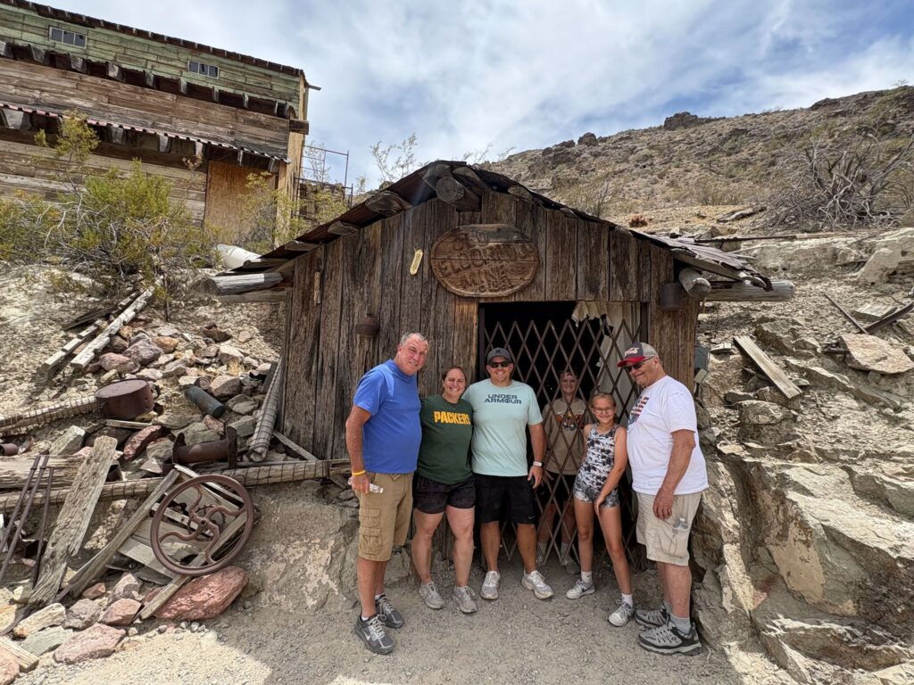 Group in front of a historic Nevada mine entrance near Las Vegas, surrounded by desert and old equipment—perfect for ATV tours.