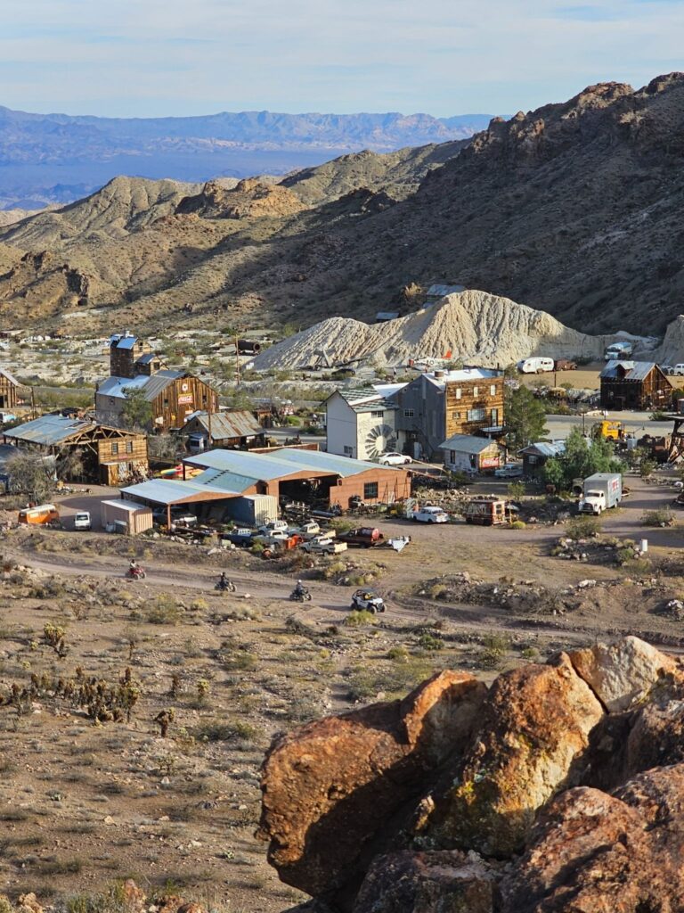 Rustic Nevada desert town near Las Vegas with tin-roof buildings, rock piles, and ATV tours amid rocky hills and sparse greenery.