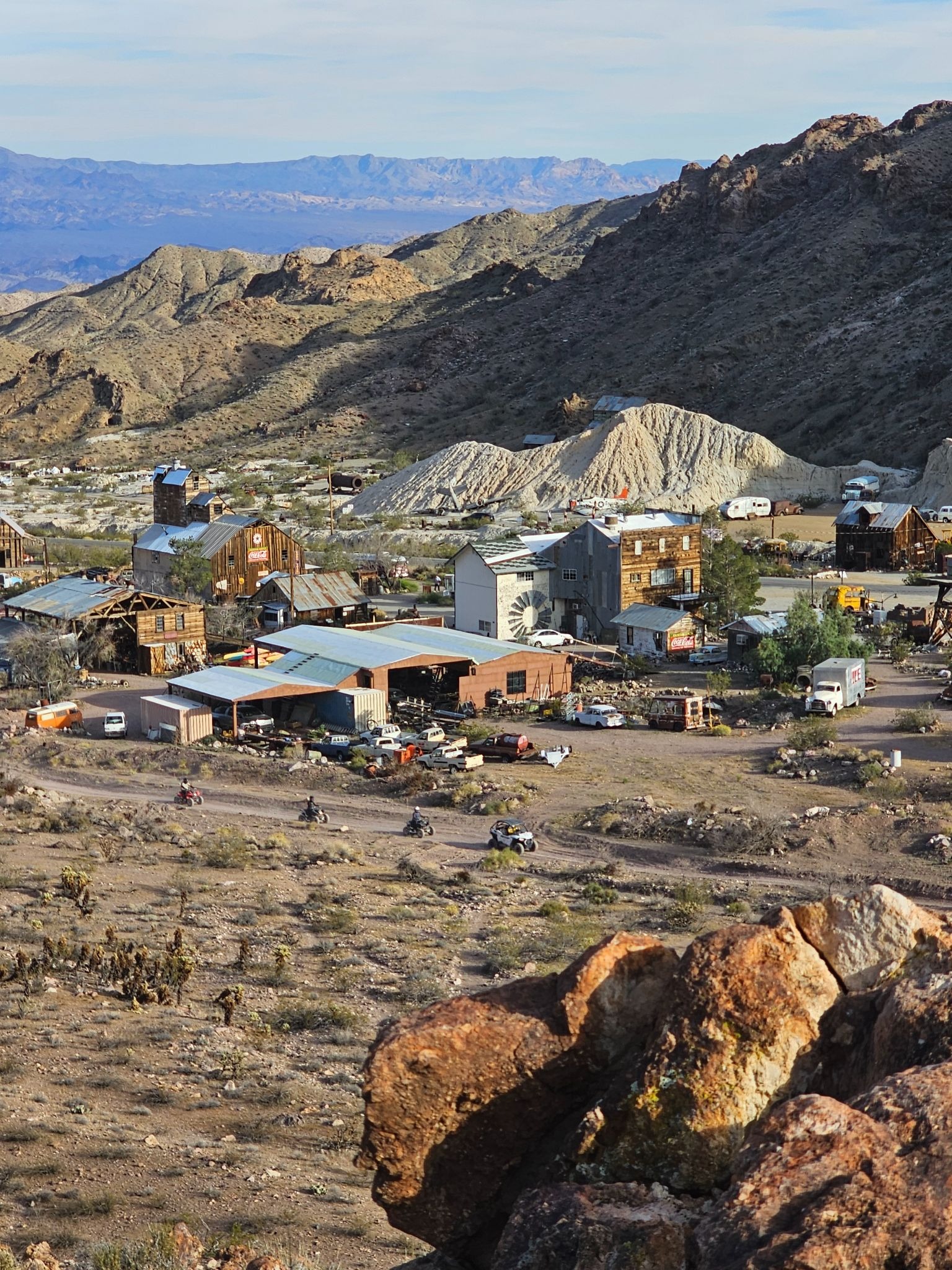 Rustic Nevada desert town near Las Vegas with tin-roof buildings, rock piles, and ATV tours amid rocky hills and sparse greenery.