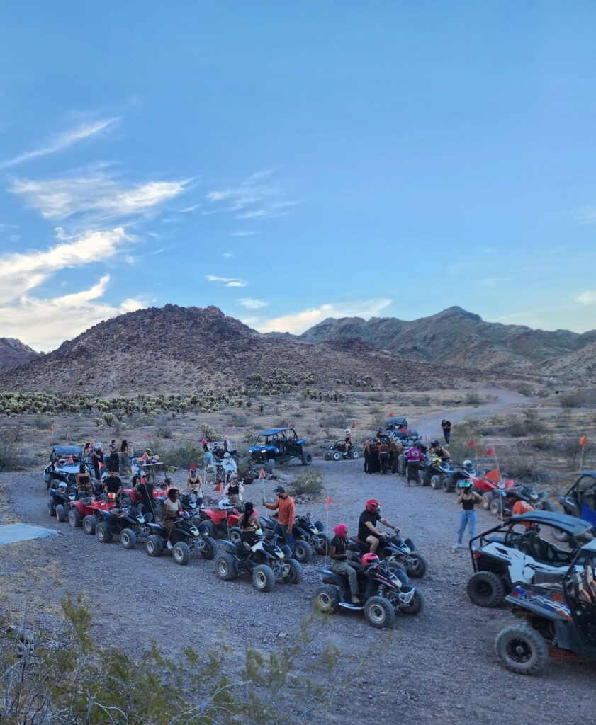 Adventurers on ATVs and RZRs explore a rocky Nevada desert trail near Las Vegas under blue skies and mountains.