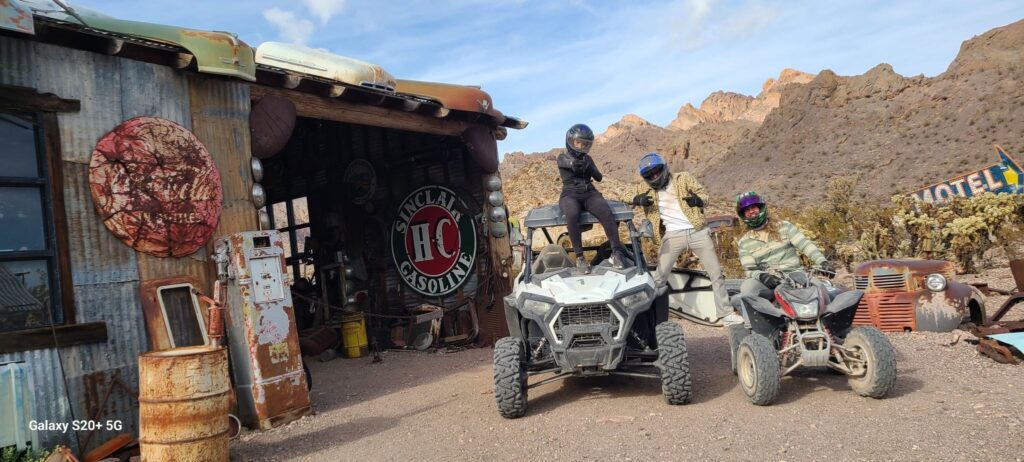 Adventurers on ATVs pose by a vintage tin building in a Nevada ghost town near Las Vegas, perfect for off-road ATV tours.